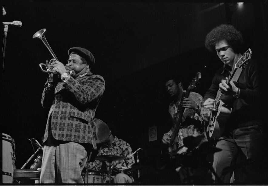 Vintage jazz band performing live on stage with trumpet, guitar, and drums.