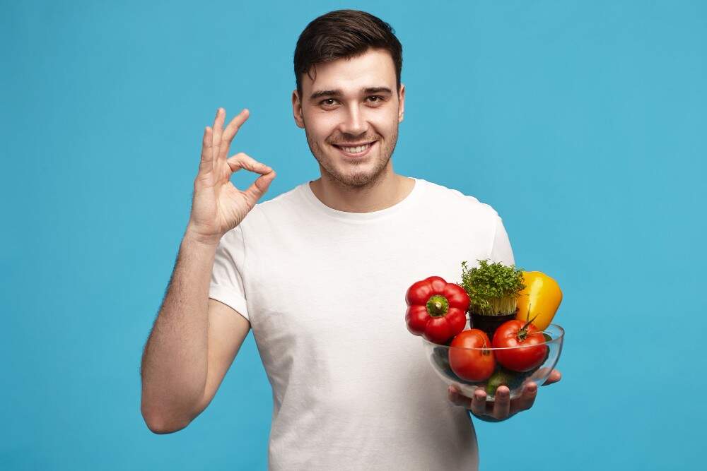 Uomo sorridente che tiene una ciotola di verdure fresche, promuovendo salute e benessere.