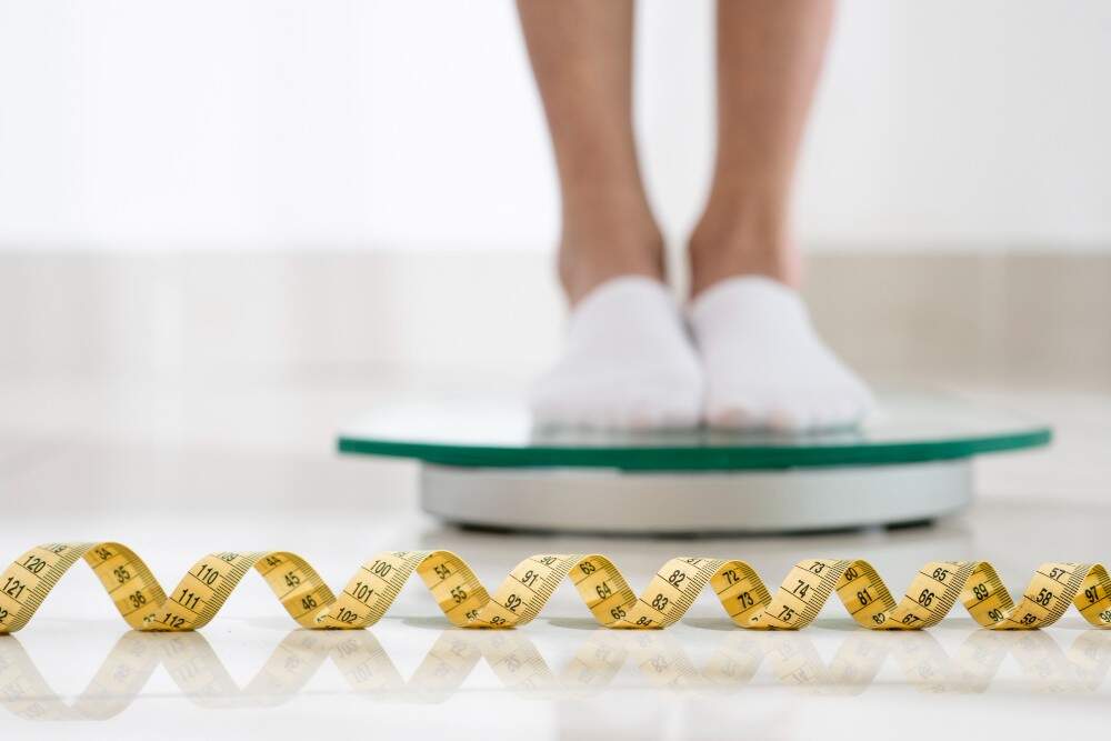 Person standing on a scale with a measuring tape in front, promoting liposuction services in Albania.