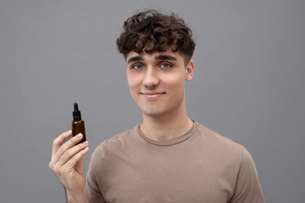 Giovane uomo che tiene una bottiglia di siero per la crescita dei capelli, promuovendo soluzioni per il ripristino dei capelli.