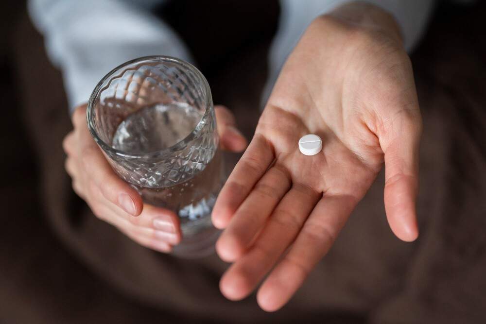Persona che tiene una pillola e un bicchiere d'acqua, promozione del turismo medico e del recupero post-chirurgico dell'orecchio in Italia.