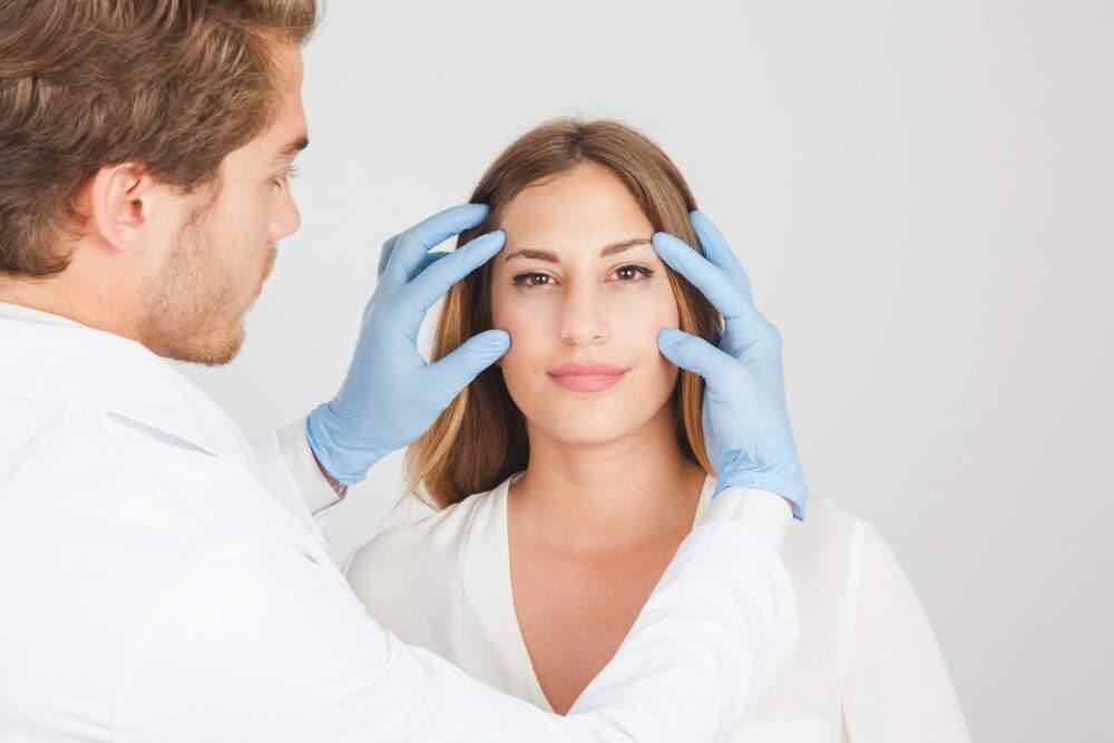 Doctor examining woman's face for facelift options in Albania.