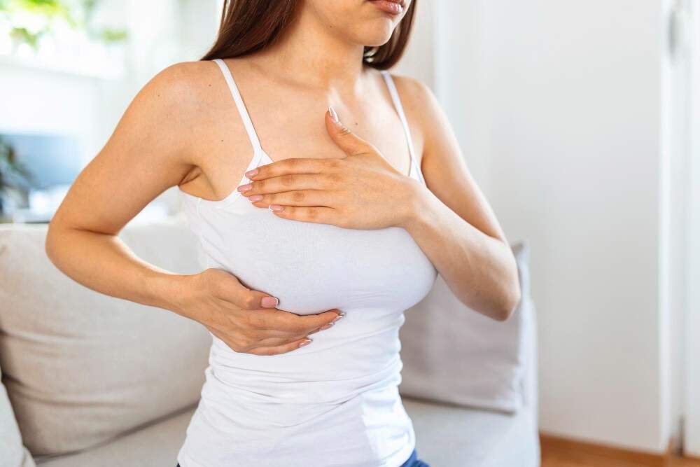 Woman holding her breast, comparing saline and silicone implants for breast augmentation.