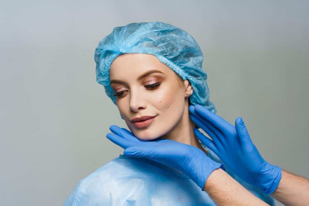 Mujer con gorro quirúrgico y guantes preparándose para una cirugía plástica en Albania.