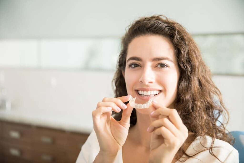 Woman holding dental veneers, showcasing cosmetic dental treatment in Albania.