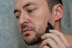 Hombre arreglándose la barba y las cejas con recortadora eléctrica, tratamiento de pérdida de cabello en Albania.
