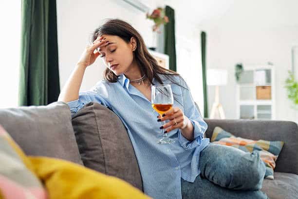 Vrouw met hoofdpijn die een glas wijn vasthoudt, gezondheidsproblemen, impact op levensstijl.