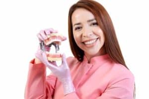 Vrouw met een model van tandheelkundige implantaten, ter presentatie van de All-on-4 en All-on-6 oplossingen.