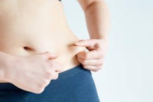 Frau kneift sich in den Bauch, Werbung für Medizintourismus in Albanien zur Gewichtsabnahme und Gesundheitsbehandlung.