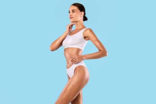 Vrouw met slank postuur in witte sportkleding tegen een blauwe achtergrond, concept voor gezondheid en welzijn.
