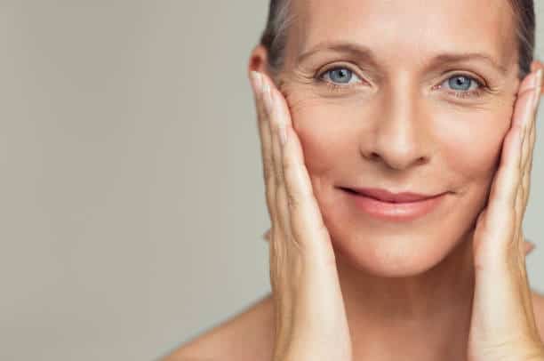 Woman with clear skin touching her face, promoting skincare and cosmetic treatments in Albania.