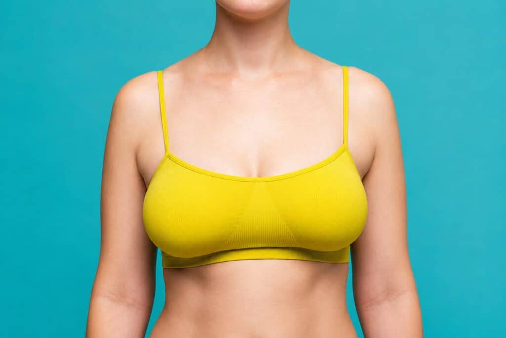 Close-up of a woman's torso in a yellow sports bra against a blue background.