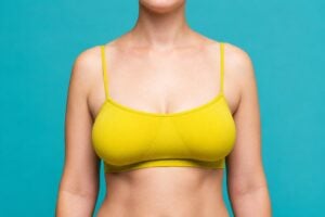 Close-up of a woman's torso in a yellow sports bra against a blue background.