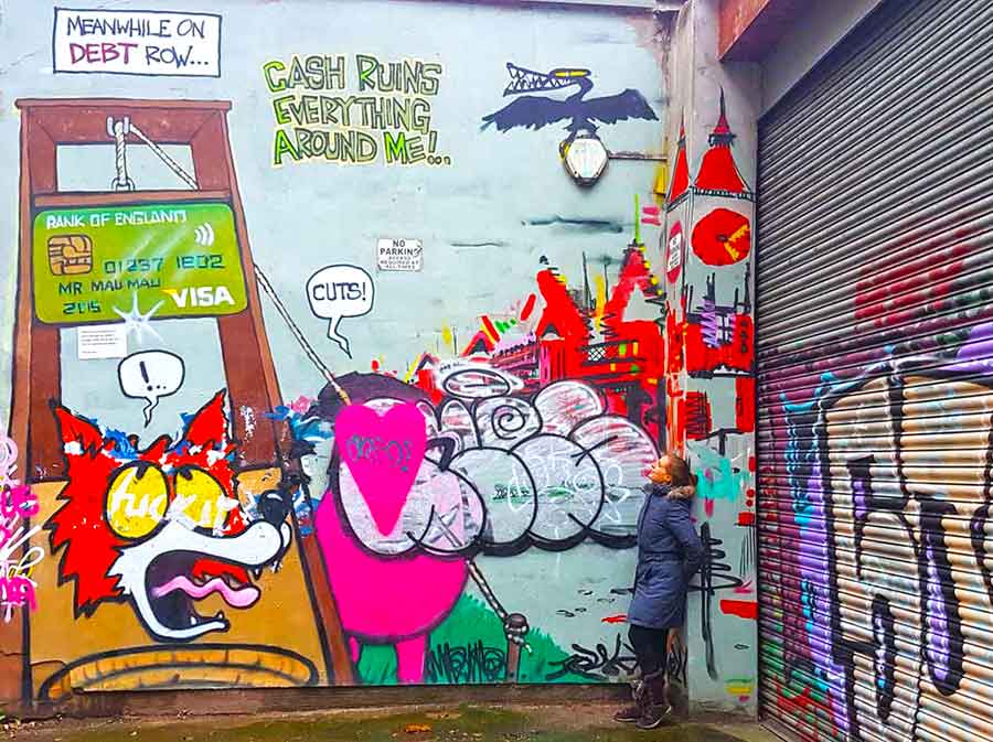 A woman standing on the corner looking at the murals painted on the walls