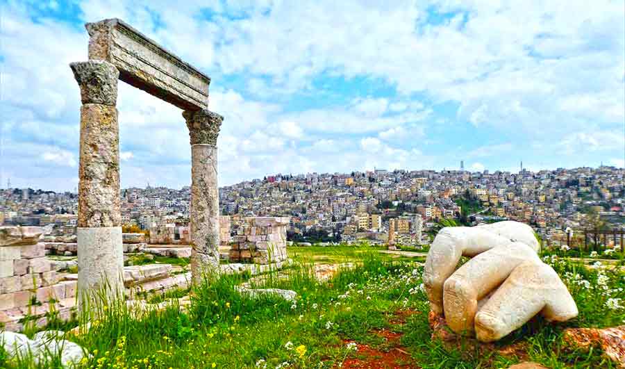 Ruins in Amman at the citadel withne columned archway and the partial reamins of a giant hand in the grass.