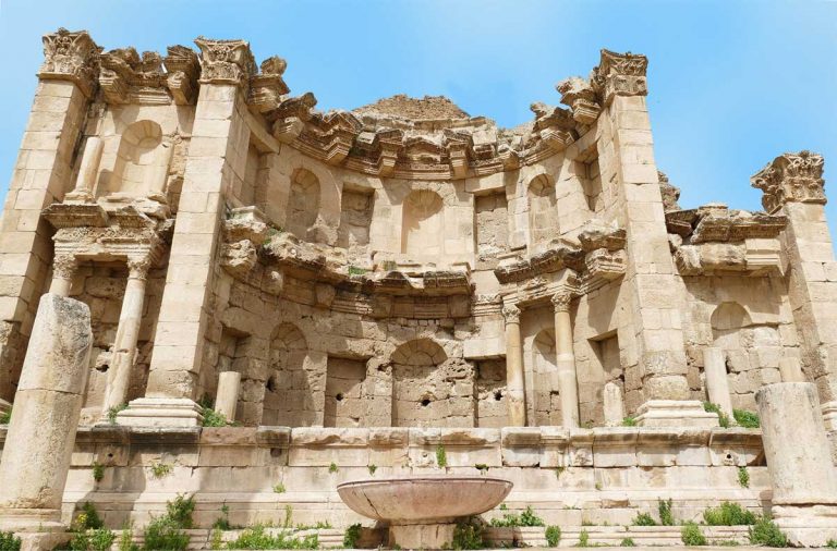 The Nymphean in Jerash, Jordan - a ruin in a semi-circular structure made of sandstone and bricks, adorned with decorative elements and featuring a fountain shrine at the center