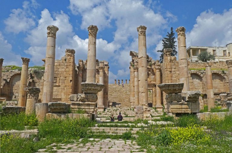 The Propylaeum - a massive decorative gateway featuring multiple old columns, large stones, and walls made of sandstone and bricks, with flowers and plants on the ground