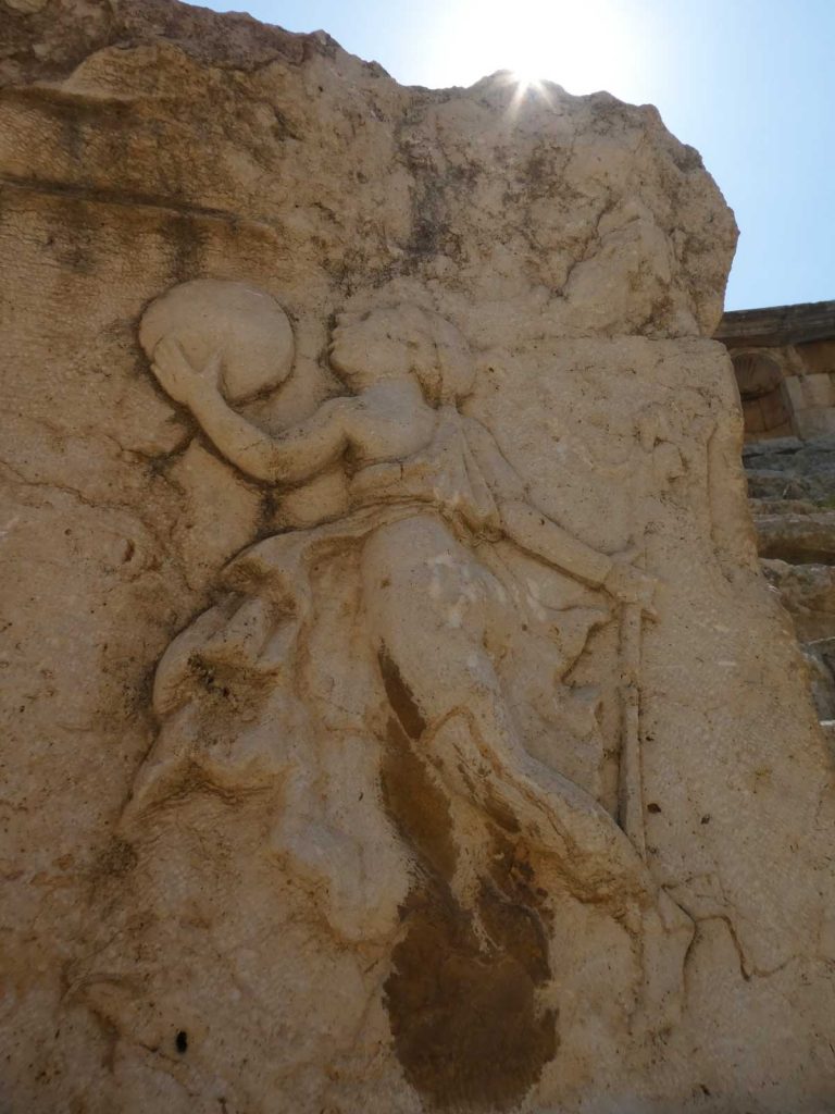 A woman carving in a large brown stone in the north theatre on a sunny day