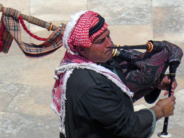 A man wearing a black long-sleeved shirt playing the bagpipes, a woodwind instrument, in Jerash, Jordan