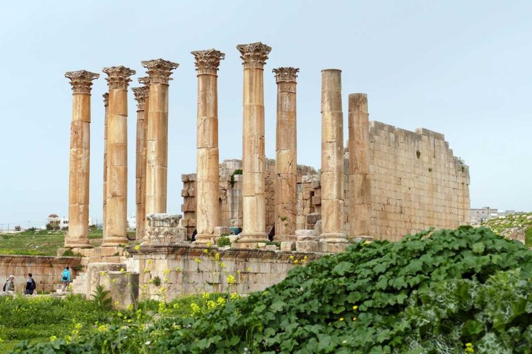 Temple of Artemis in Jerash, Jordan, featuring Greek architecture surrounded by a single row of columns, old brick walls; lush green plants at the side of the ruins