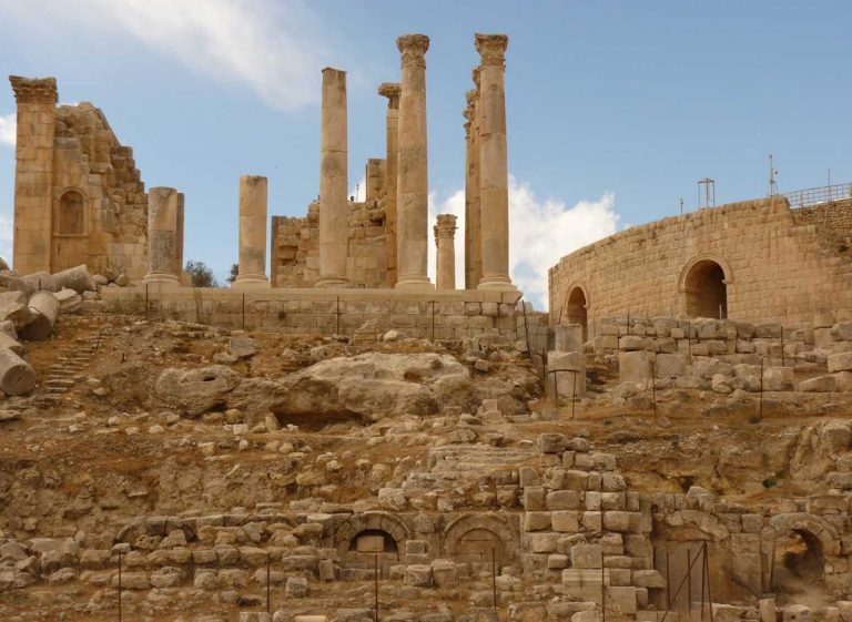 Temple of Zeus in Jerash, Jordan, a massive structure perched on top of old structured stones, featuring a colonnade of columns and a brickstone building at the side
