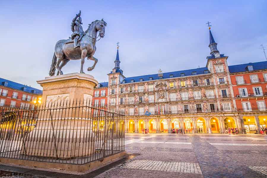 Madrid In Winter: Over 30 Things to Do In Winter in Madrid 7 Plaza Major in Madrid at dusk with the statue of the hourse and soldier in the middle and surrounded by lit alcoves of the buildings.
