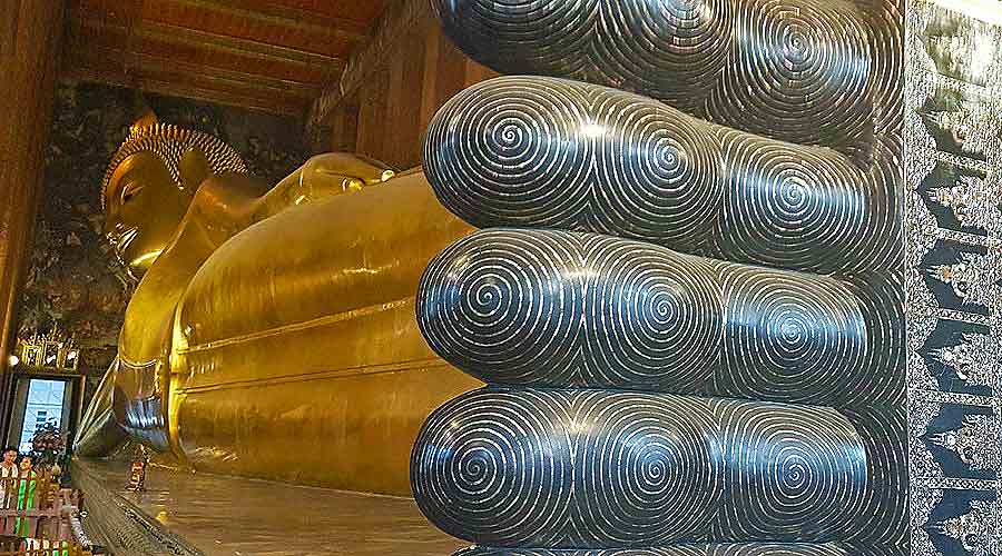 The Golden Reclining Buddha at Wat Pho features Buddha lying on his side, with his hand supporting his head, inside a temple