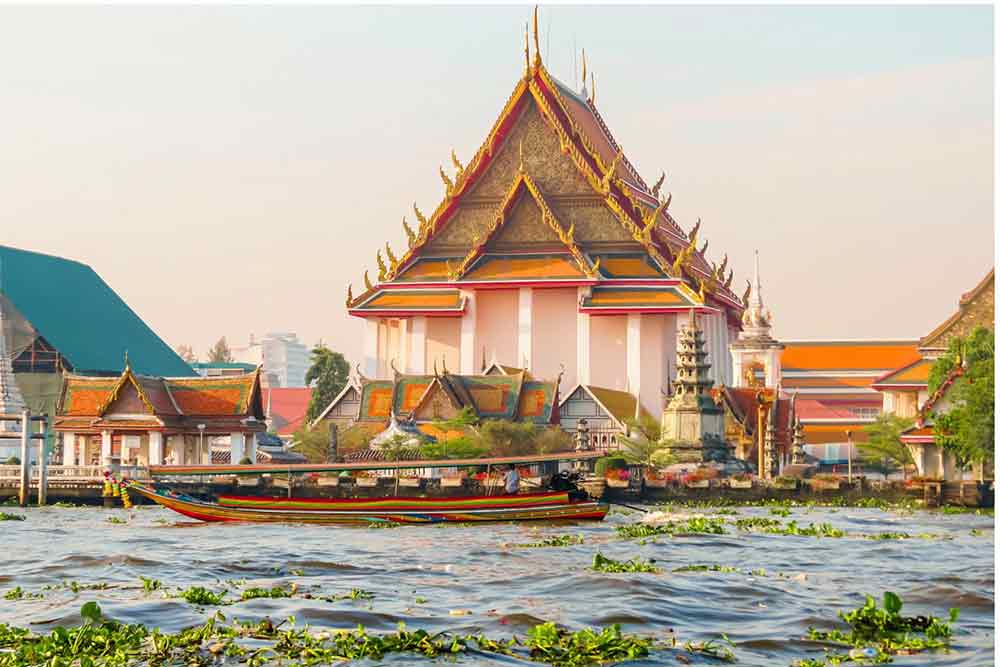 The Chao Phraya Rivre with buildings along hte far bank and a boat in the forground. 