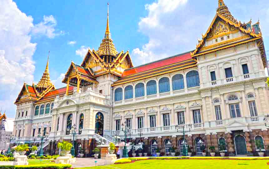 Grand Palace in Bangkok features a large palace with multi-tiered roof and spires surrounded by well-maintain lawn and gardens