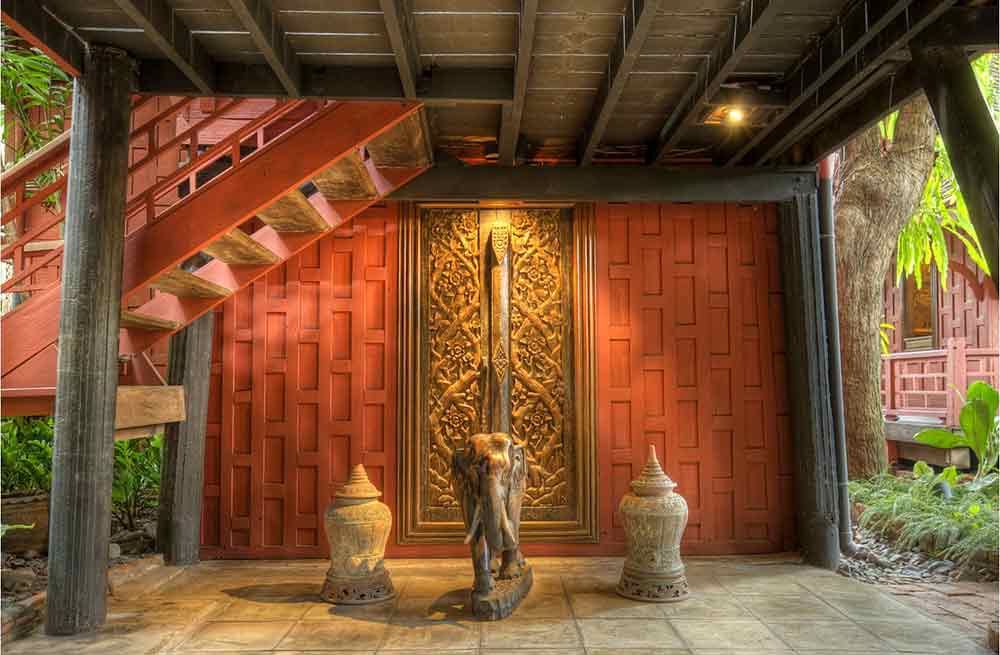 A traditional Thai house with decorative walls and three statues on the floor. The middle on is an elephant, the side two are urns. 