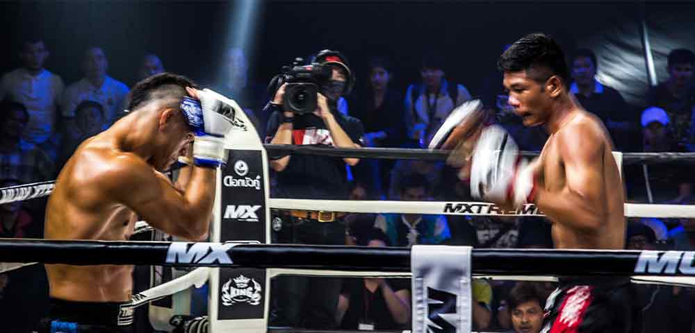 Two men in a Muay Thai match with a camera man in the background. 