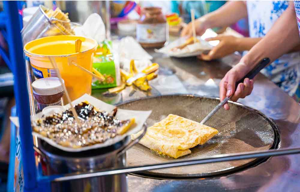 A street vendor making roti with chocolate and banana.