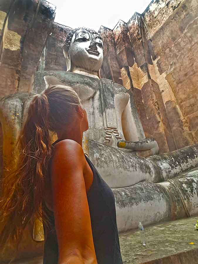 A woman taking a selfie admiring the large seated Buddha at Sukhotai Ruins in Thailand
