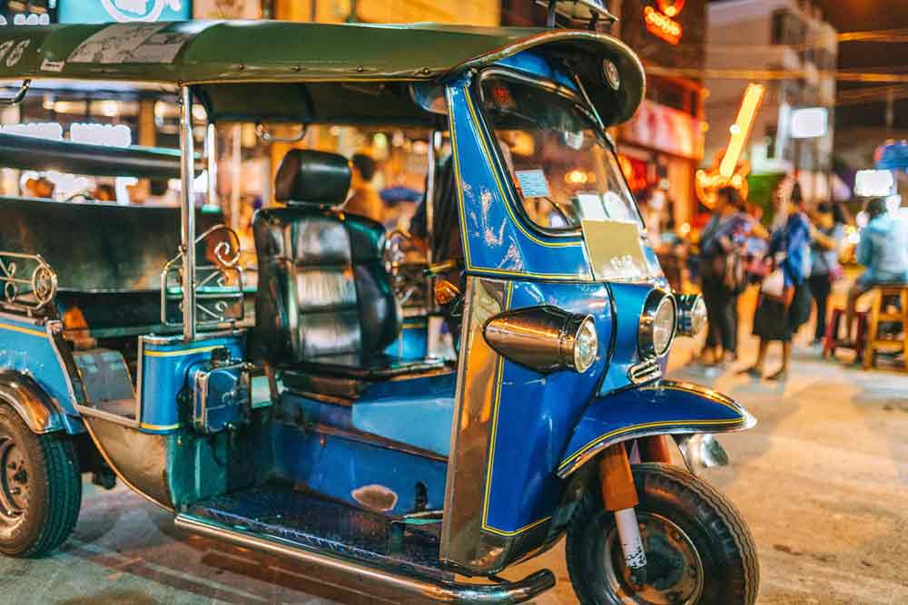 A metallic blue TukTuk in a street in Bangkok.
