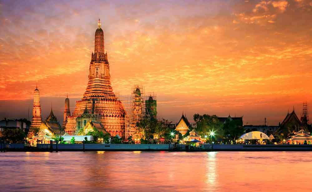 The temple of Wat Arun and an orange sky with the river in the forground. 