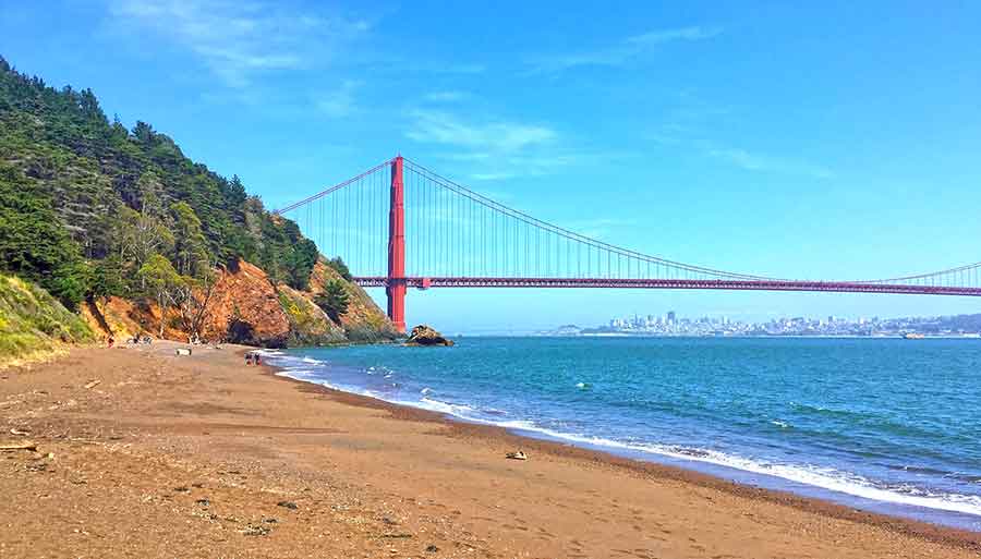 33 Best Hidden Coves and Secluded Beaches Around the World 14 Kirby Cove in San Francisco, USA, provides a scenic view of the iconic Golden Gate Bridge, framed by the blue waters below, while the shoreline is adorned with brown sand.