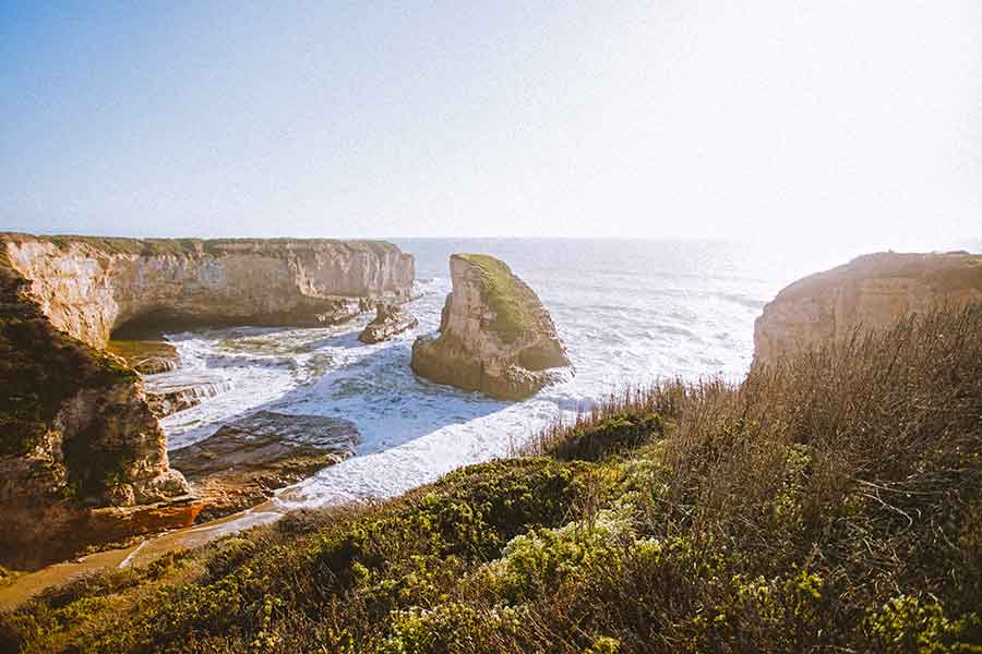 33 Best Hidden Coves and Secluded Beaches Around the World 12 Shark Fin Cove in San Francisco, USA, showcases a distinctive rock formation resembling a shark fin at its center, while ocean waves gently lap against the shoreline on a bright sunny day.