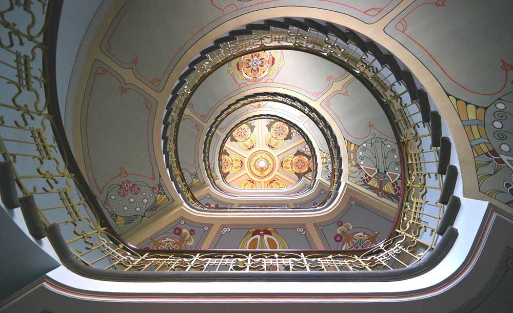 Best Riga 3 Days Itinerary: Exploring ‘Paris of the North’ 22 Looking up at a starcase in the Art Nouveu museum in Riga The underside of the staircase is decorated with flowers nad swirling borders.