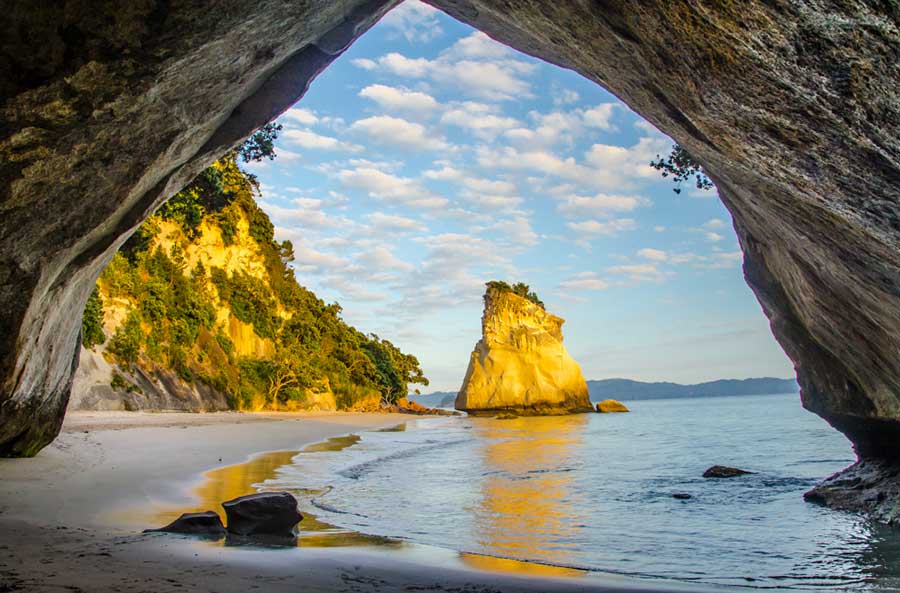 33 Best Hidden Coves and Secluded Beaches Around the World 29 From the tunnel cave at Cathedral Cove, New Zealand, a breathtaking scene unfolds: the sea, its gentle waves lapping against the brown sands