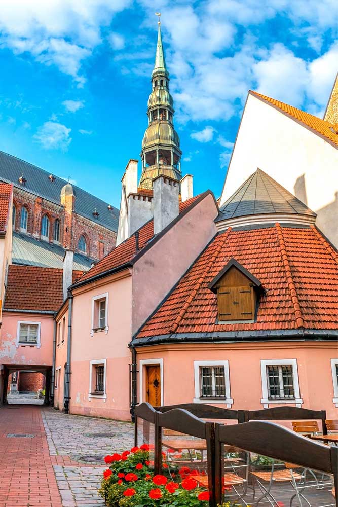Best Riga 3 Days Itinerary: Exploring ‘Paris of the North’ 6 The pretty buildings of Konvents Seta. In the forground is a round pink building, and the church spire in the background.