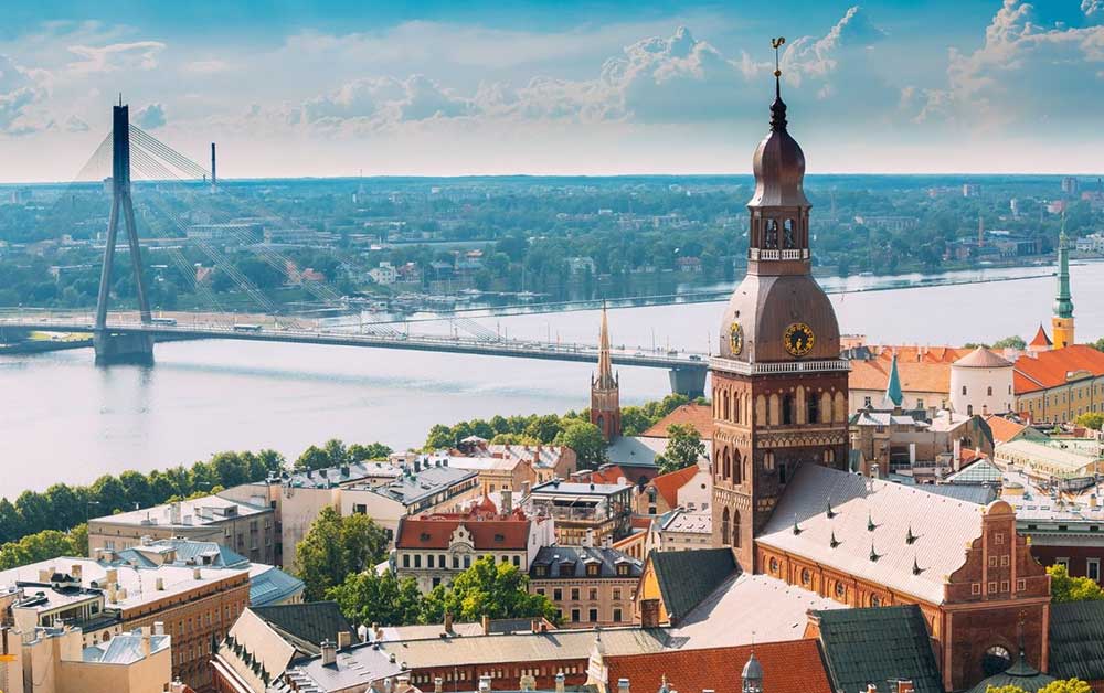 Best Riga 3 Days Itinerary: Exploring ‘Paris of the North’ 1 View of Riga with a church spire in the foreground and the old town. In the background are a river and a modern bridge.