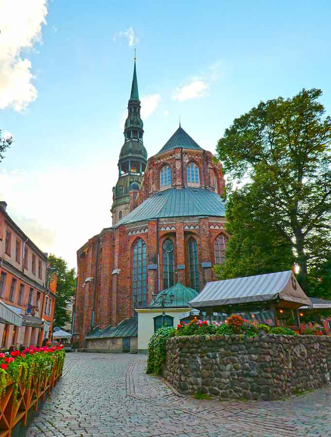Best Riga 3 Days Itinerary: Exploring ‘Paris of the North’ 4 Riga 3 days guide be sure to visit St Peters Church tower. The image shows the church with flowers in the forground.