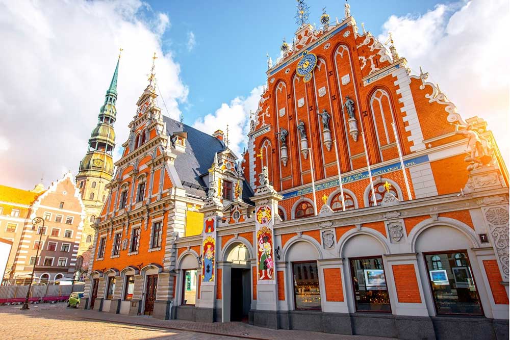 Best Riga 3 Days Itinerary: Exploring ‘Paris of the North’ 3 The ornate red building of the House of the Blackheads in Riga with blue skies and a church spire in the background.