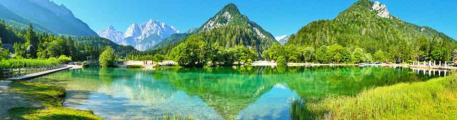 Jasna Lake in Slovenia features an emerald green waters surrounded by lush trees and mountains on the background