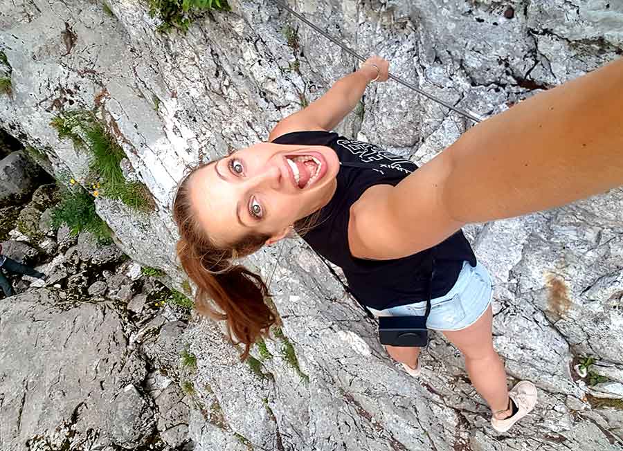 A woman in black sleeveless climbing up on a gray limestone cliff to see the source of the Soca River