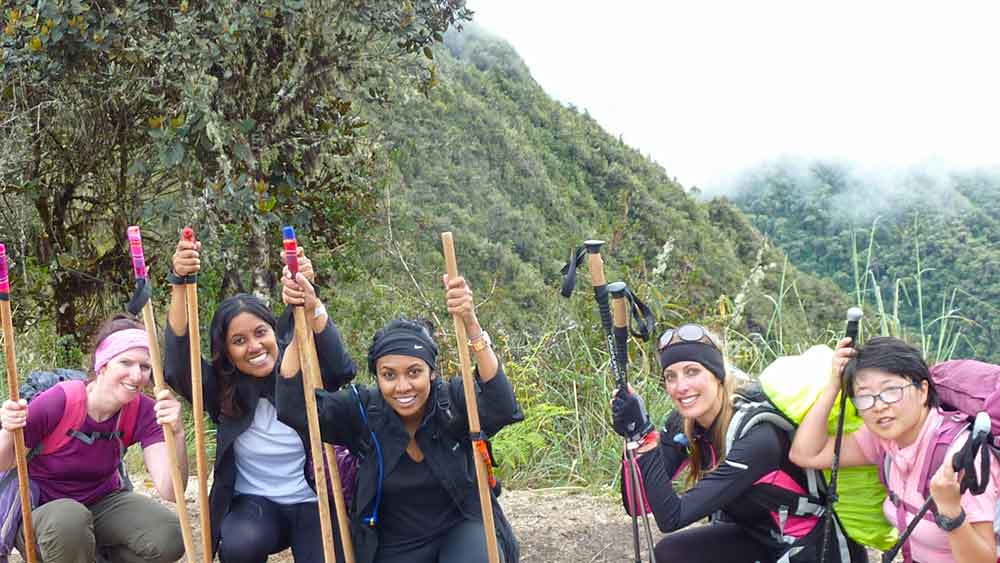 G Adventures Inca Trail Review: What to Expect on The Inca Trail Trek to Machu Picchu 6 Group of 5 women (one of them is me) crouched down and holding walking ples in front on the misty bacground of the Sacred Valley