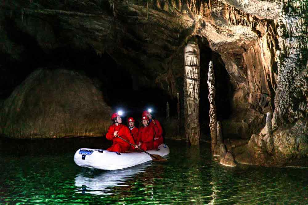 Extreme Adventures in Europe: 29 Best Adventure Sports in Europe 13 Four tourists wearing red suits are onboard a boat, exploring kayaking at the underground lakes of Krizna Jama in Slovenia