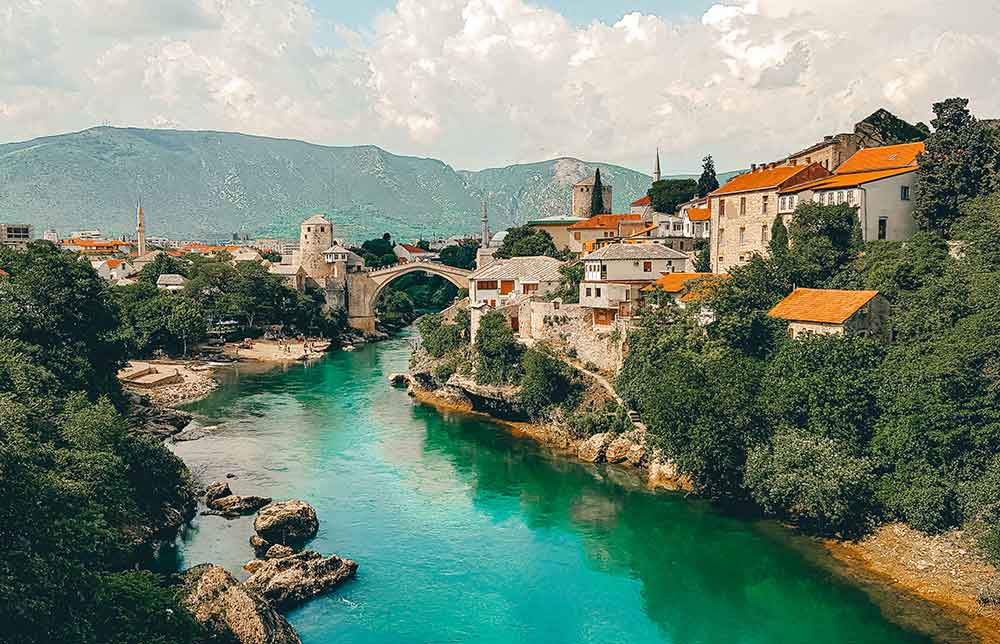Extreme Adventures in Europe: 29 Best Adventure Sports in Europe 3 The Mostar Bridge with an overflowing water surrounded by trees and houses