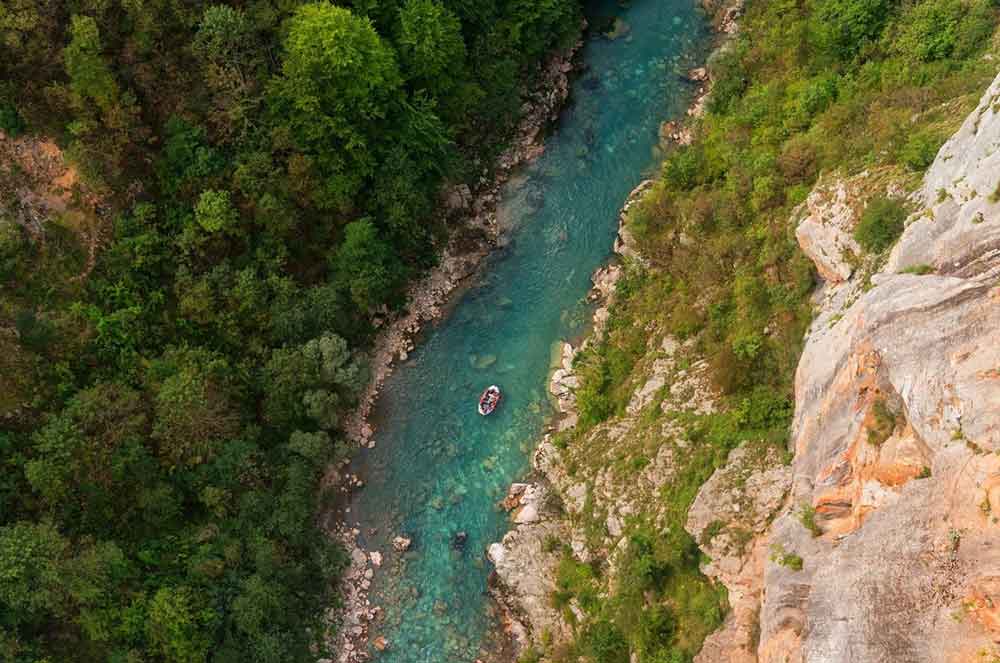 Birds eye view of a blue river in a green forest with a small raft on it.
