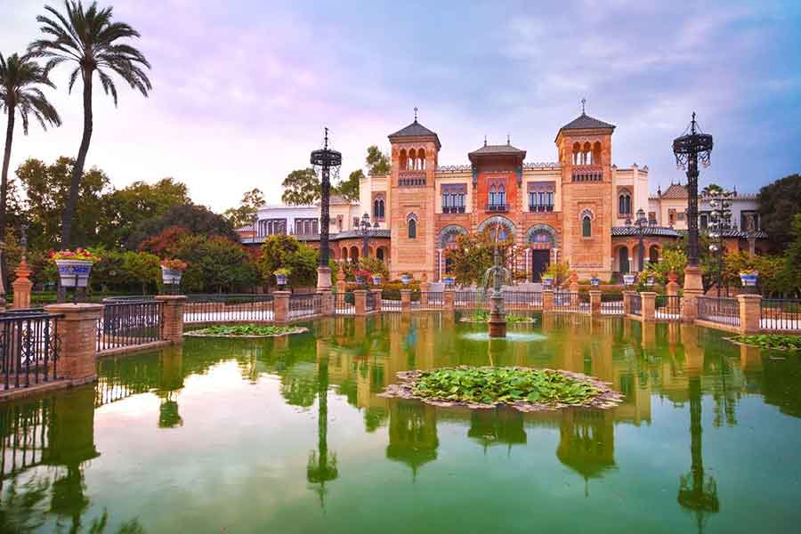 An ornate building of the Museuo de Artes y Costumbres refecing in a pond. 